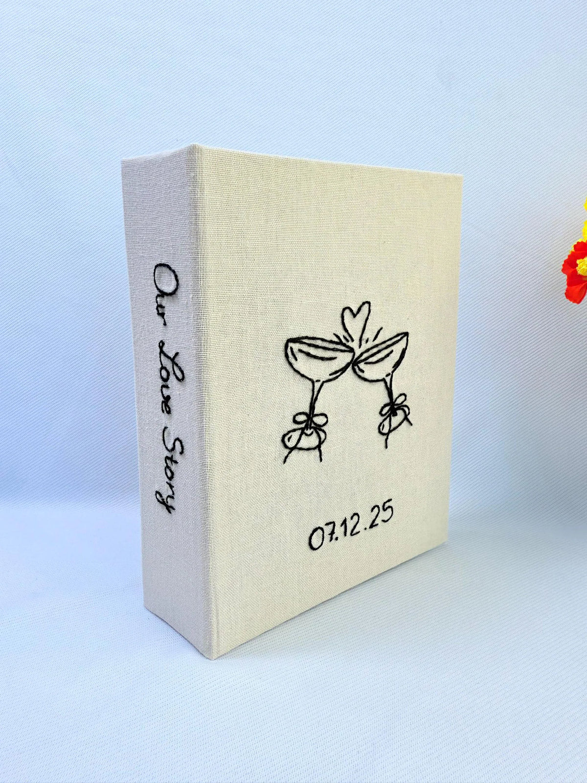 A beige photo album with black embroidered line art and Our Love Story on the spine — hand-embroidered by The Thread Nest