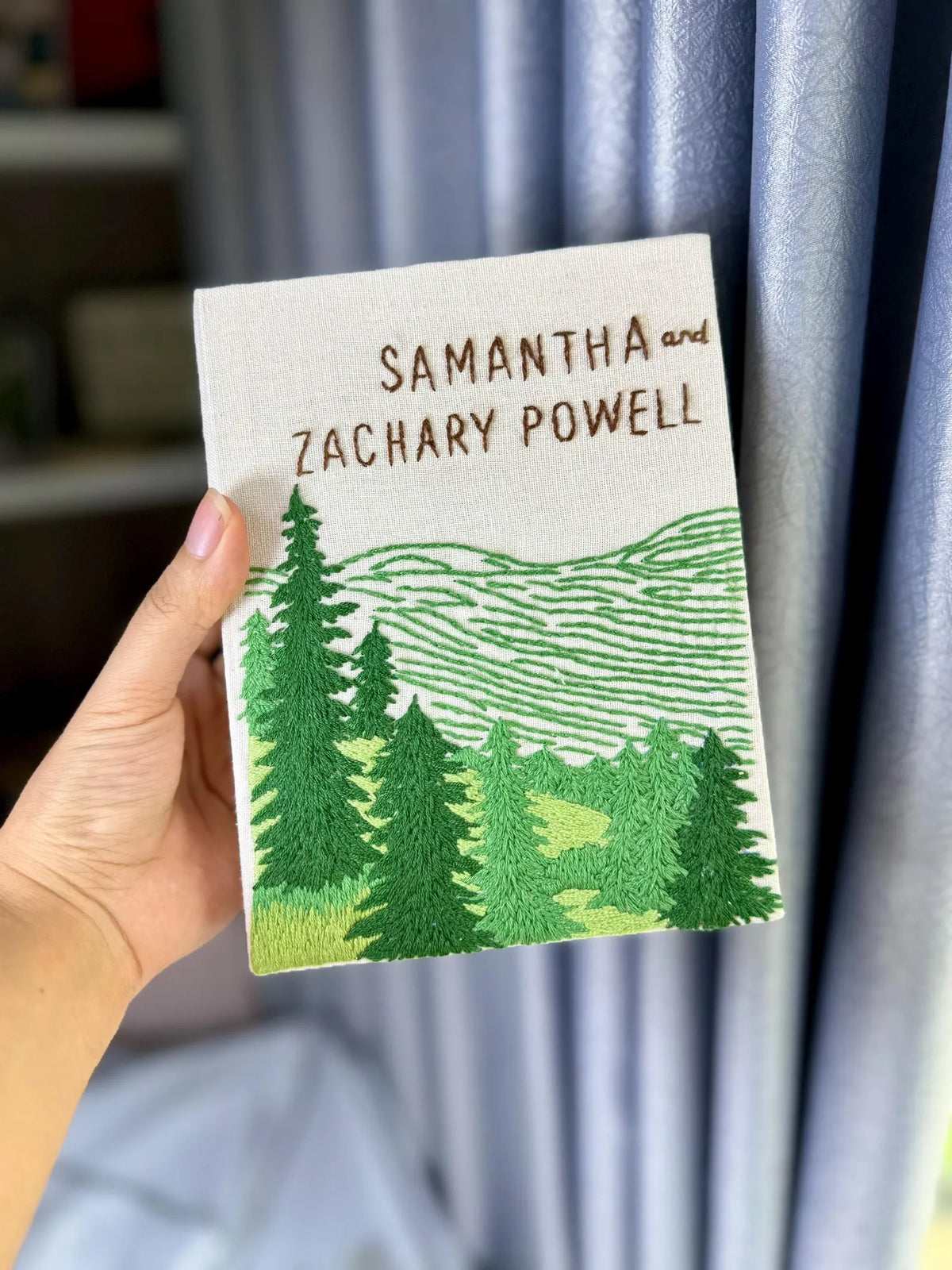 An embroidered cover with two names, a green forest and mountain design — hand-embroidered by The Thread Nest