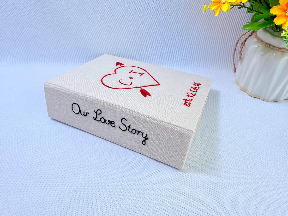 An off-white keepsake box with Our Love Story embroidered in black on the side — hand-embroidered by The Thread Nest