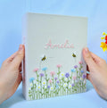 A light gray photo album with a name in pink script and embroidered flowers — hand-embroidered by The Thread Nest