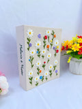 A beige canvas with embroidered white daisies and two stitched names — hand-embroidered by The Thread Nest
