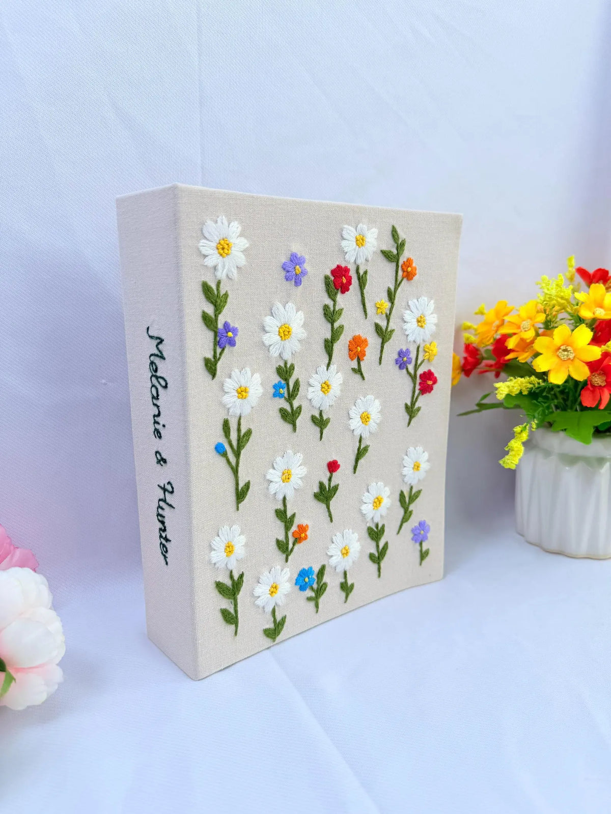 A beige canvas with embroidered white daisies and two stitched names — hand-embroidered by The Thread Nest