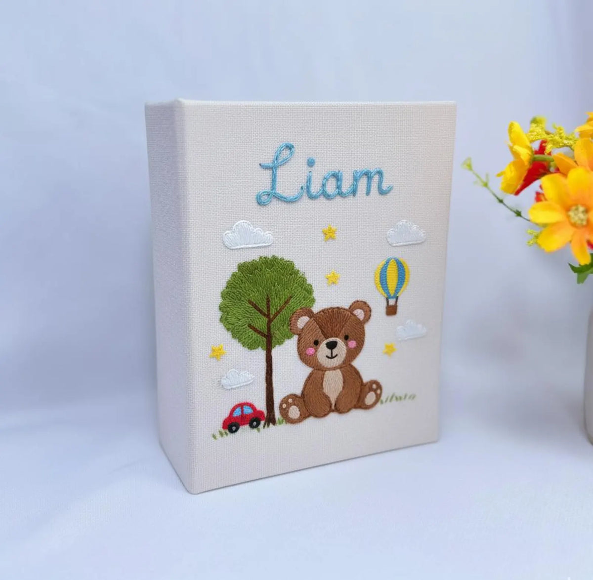 A cream-colored keepsake box with a stitched name, a teddy bear and a red car — hand-embroidered by The Thread Nest