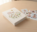 A white photo album with embroidered flowers in green, pink and yellow and the name Mia — hand-embroidered by The Thread Nest