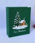 A green book with an embroidered snow-covered house and evergreen tree — hand-embroidered by The Thread Nest