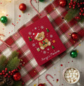 A red Christmas journal with an embroidered teddy bear in a Santa hat — hand-embroidered by The Thread Nest