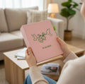 A light pink cover with dark green line art of two birds and two hearts — hand-embroidered by The Thread Nest