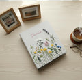 A light gray photo album with a name in pink and an embroidered floral design — hand-embroidered by The Thread Nest
