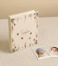 A cream-colored baby photo album with floral embroidery and a name in script — hand-embroidered by The Thread Nest