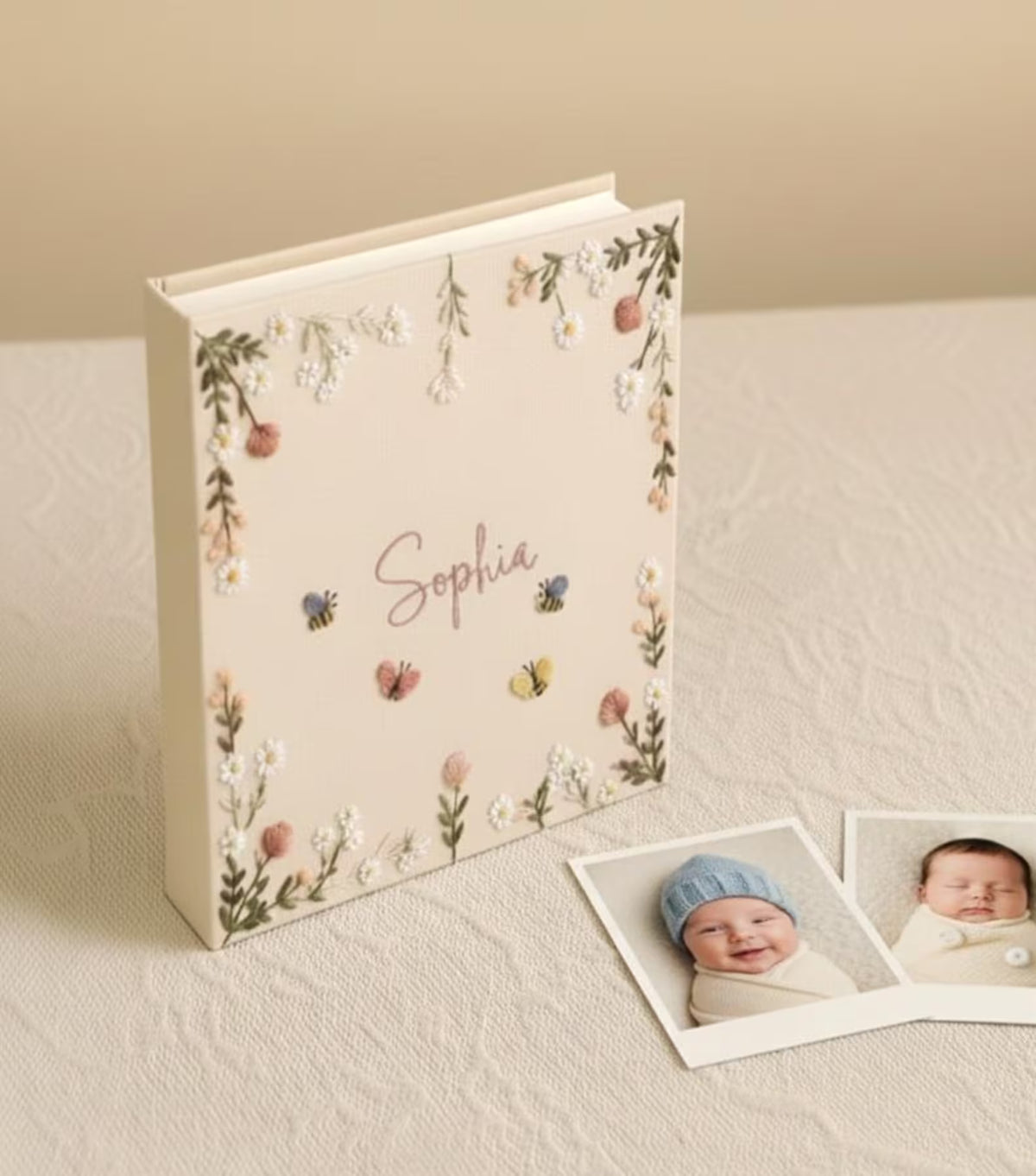 A cream-colored baby photo album with floral embroidery and a name in script — hand-embroidered by The Thread Nest
