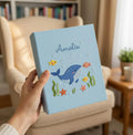 A light blue book with an embroidered blue whale, fish and seaweed — hand-embroidered by The Thread Nest