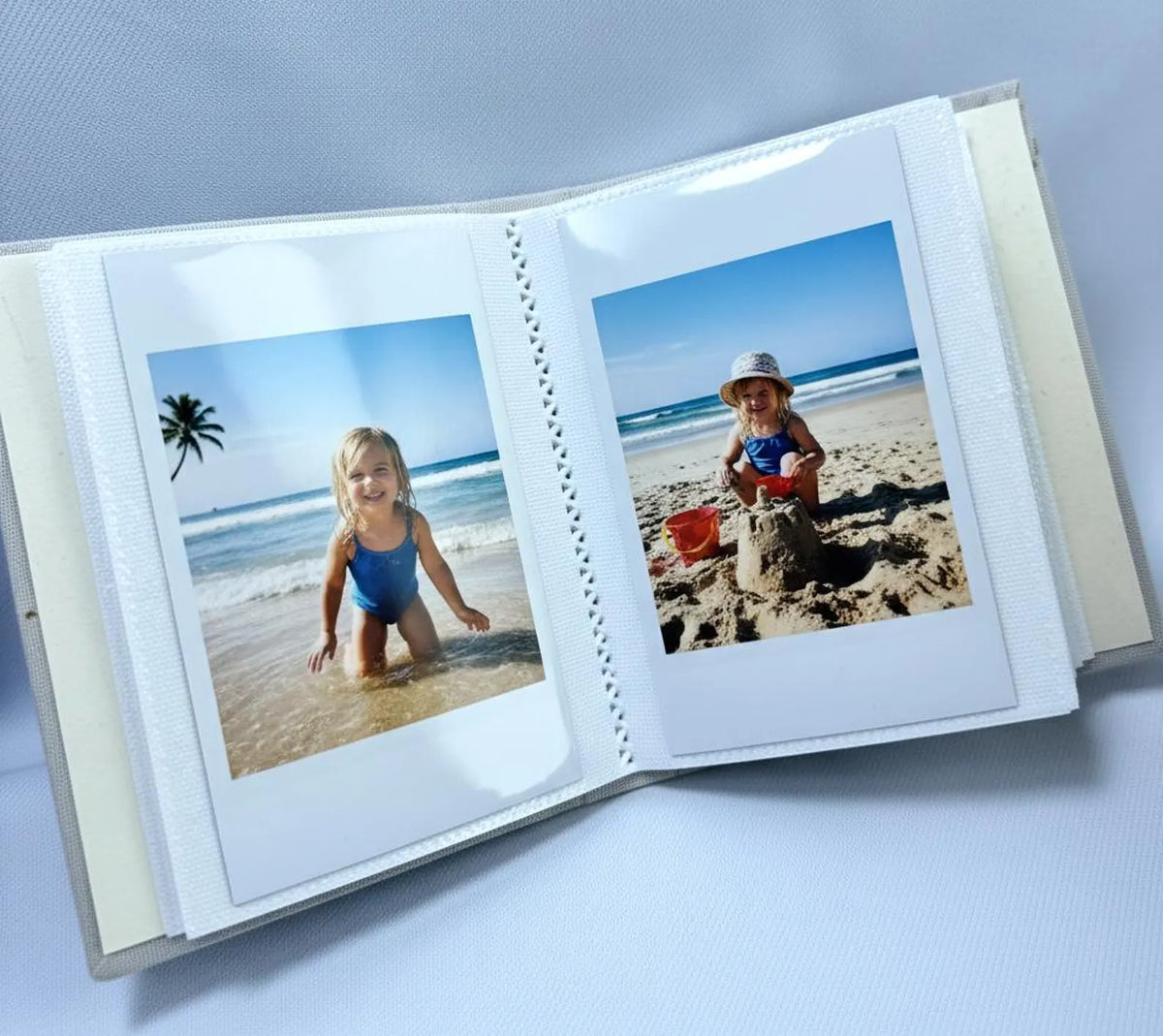 An open photo album showing two beach photographs — hand-embroidered by The Thread Nest