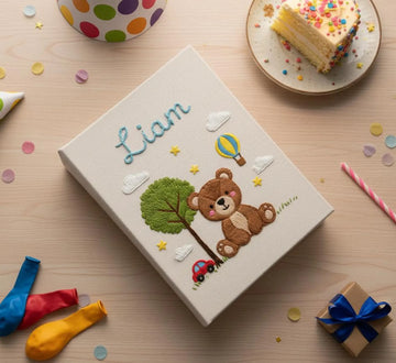 A cream-colored cover with a stitched name, a teddy bear, a tree and a red car — hand-embroidered by The Thread Nest