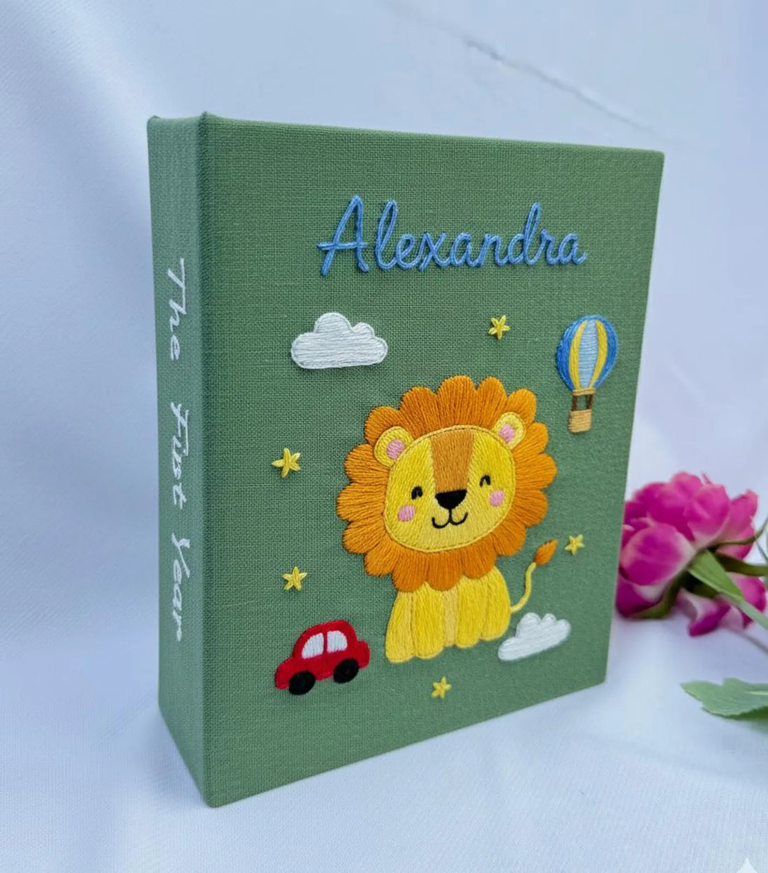 A cream-colored cover with a stitched name, a teddy bear, a tree and a red car — hand-embroidered by The Thread Nest