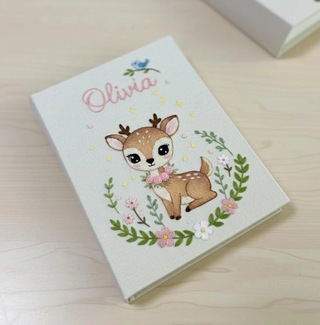 A white notebook with an embroidered fox under a green tree with red mushrooms — hand-embroidered by The Thread Nest