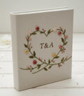 A light gray photo album with an embroidered heart-shaped wreath of pink roses — hand-embroidered by The Thread Nest
