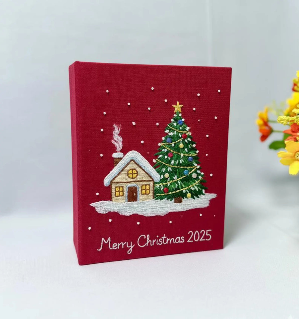 A red Christmas canvas with a snow-covered house and a decorated tree — hand-embroidered by The Thread Nest