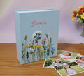 A light blue photo album with a name in pink and embroidered wildflowers — hand-embroidered by The Thread Nest