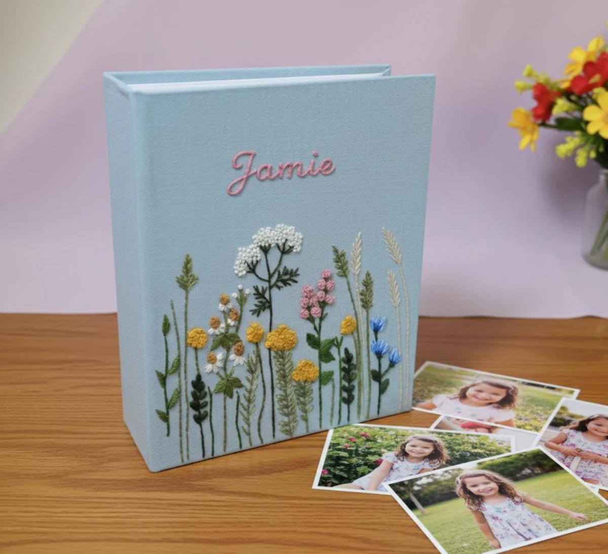 A light blue photo album with a name in pink and embroidered wildflowers — hand-embroidered by The Thread Nest