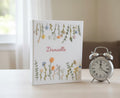 A white book with embroidered flowers and a name in red script — hand-embroidered by The Thread Nest