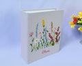A light beige book with an embroidered floral design in yellow, pink, white and red — hand-embroidered by The Thread Nest