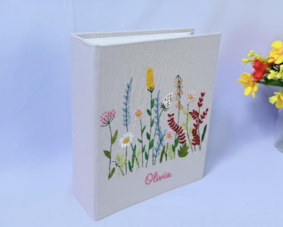 A light beige book with an embroidered floral design in yellow, pink, white and red — hand-embroidered by The Thread Nest