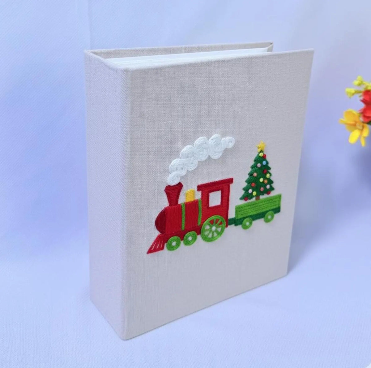 A light beige photo album with an embroidered Christmas train — hand-embroidered by The Thread Nest