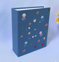 A blue book with embroidered jellyfish, starfish and seaweed — hand-embroidered by The Thread Nest