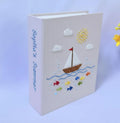 A light pink photo album with an embroidered sailboat, sun and clouds — hand-embroidered by The Thread Nest