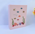 A pink canvas with an embroidered underwater scene of fish, snails and coral — hand-embroidered by The Thread Nest