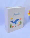A light beige book with an embroidered whale and sea life — hand-embroidered by The Thread Nest