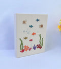A cream-colored canvas with an embroidered underwater scene — hand-embroidered by The Thread Nest