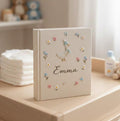 A cream-colored photo album with an embroidered white duck in a blue hat and scarf — hand-embroidered by The Thread Nest