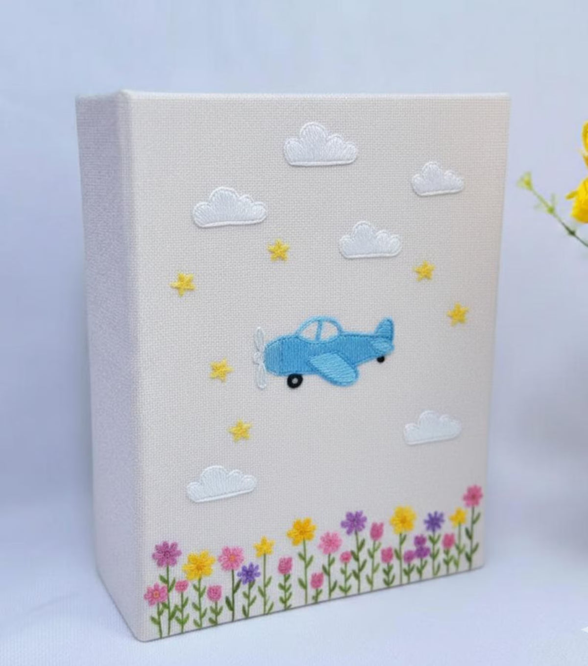 A light beige photo album with a central embroidered airplane — hand-embroidered by The Thread Nest