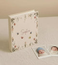 A cream-colored photo album with embroidered floral borders, small bees and butterflies — hand-embroidered by The Thread Nest