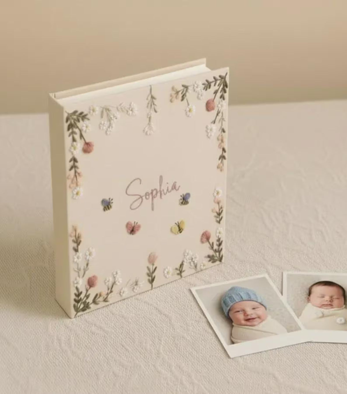 A cream-colored photo album with embroidered floral borders, small bees and butterflies — hand-embroidered by The Thread Nest