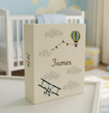 A cream-colored photo album with embroidered clouds, a hot air balloon and a biplane — hand-embroidered by The Thread Nest