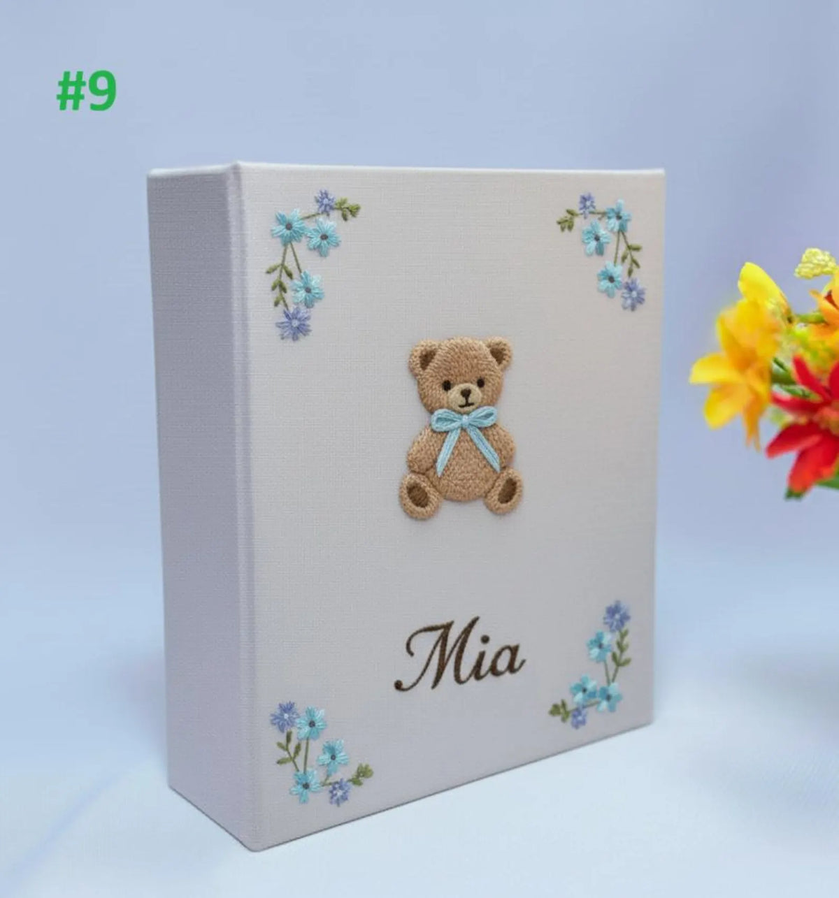 A light keepsake box with a brown teddy bear in a blue bow and blue flowers — hand-embroidered by The Thread Nest