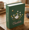 A green book with an embroidered white goose, daisies and a bee — hand-embroidered by The Thread Nest