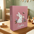 A pink baby memory book with an embroidered white bunny holding a flower — hand-embroidered by The Thread Nest