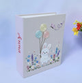 A light beige book with an embroidered white bunny holding balloons — hand-embroidered by The Thread Nest