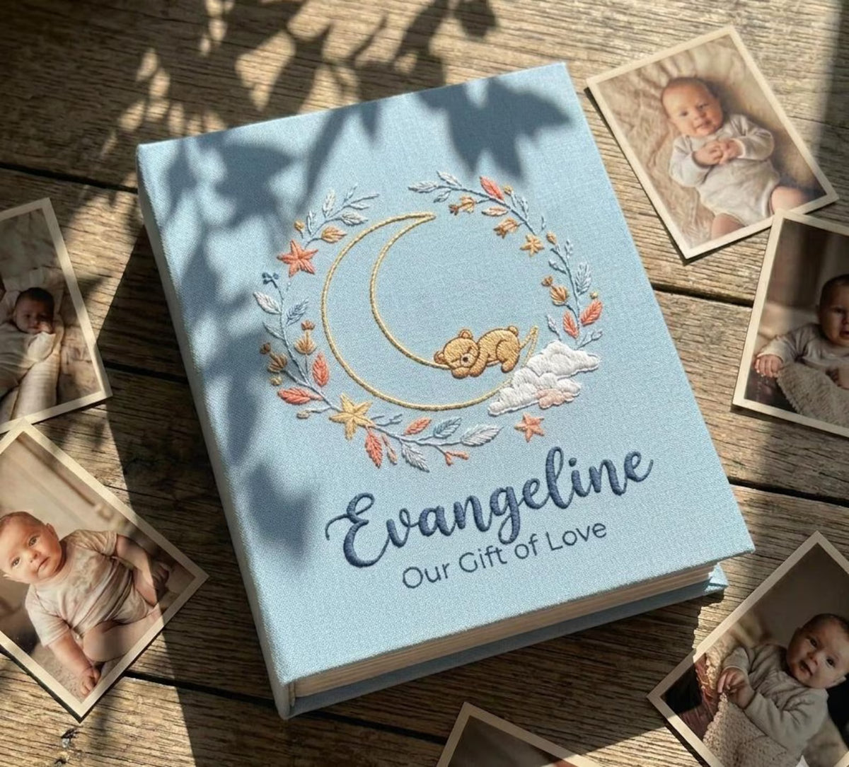 A light blue photo album with an embroidered crescent moon, a bear and a floral wreath — hand-embroidered by The Thread Nest