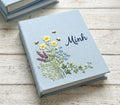 A light blue journal with embroidered wildflowers and two small bees — hand-embroidered by The Thread Nest