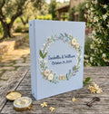 A light blue binder with an embroidered floral wreath, names and a date — hand-embroidered by The Thread Nest