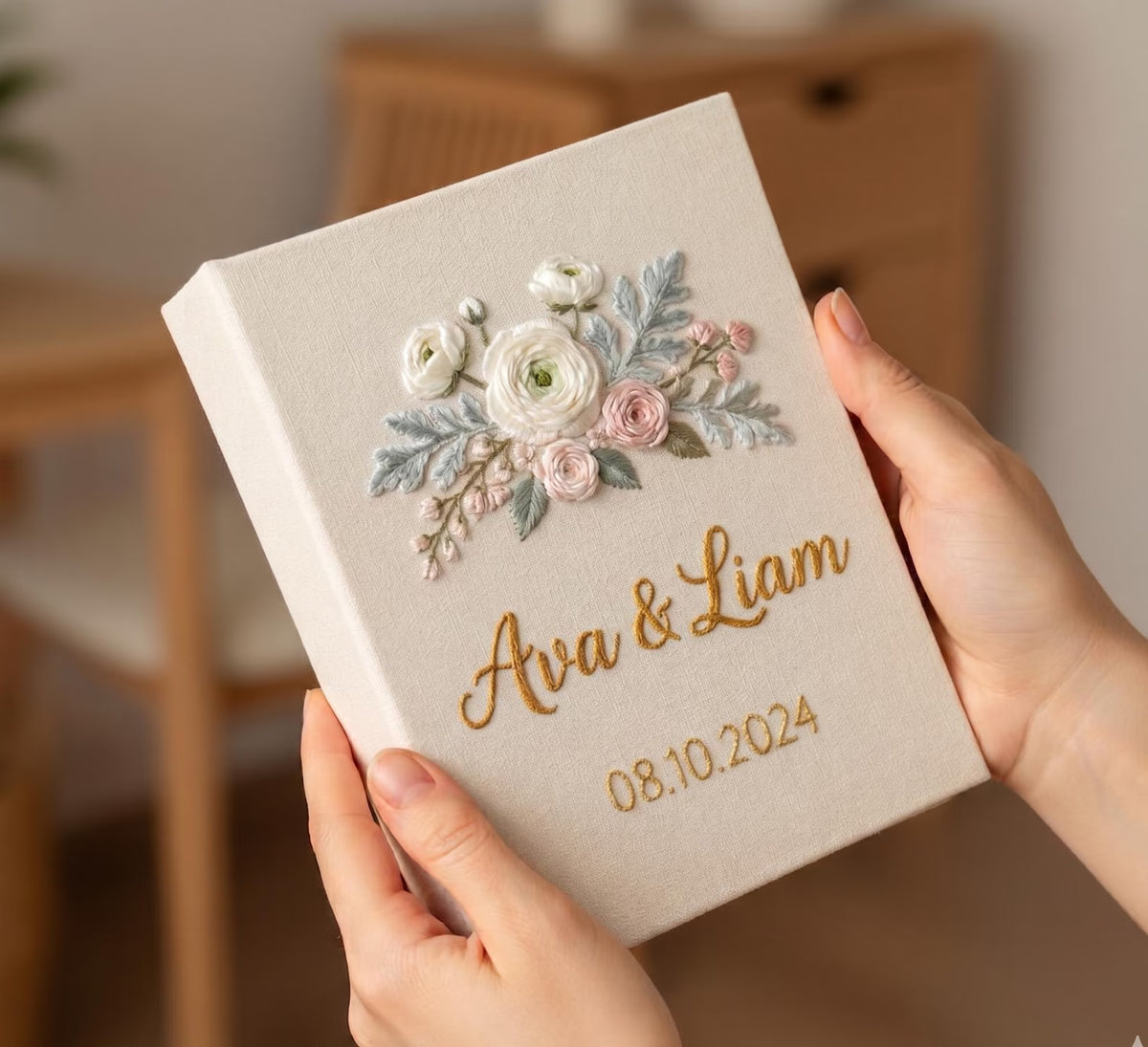 A cream-colored book with an embroidered floral arrangement in white, pink and sage — hand-embroidered by The Thread Nest
