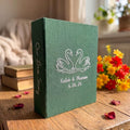 A forest green photo album with white embroidered swan silhouettes — hand-embroidered by The Thread Nest
