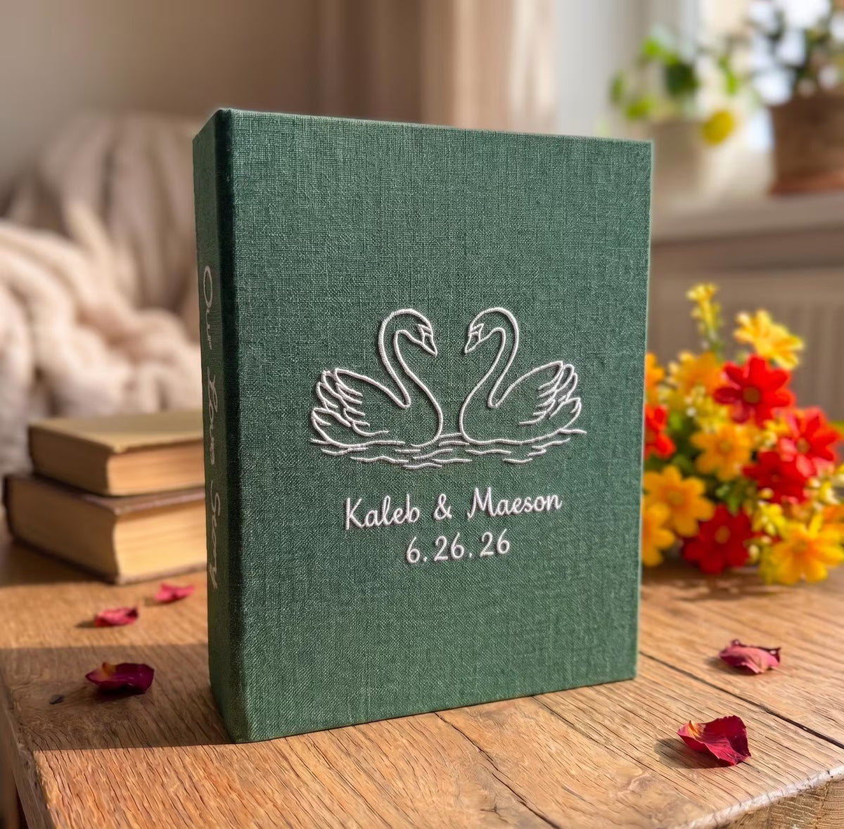 A forest green photo album with white embroidered swans facing each other — hand-embroidered by The Thread Nest