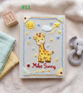 An embroidered baby book with a yellow giraffe, a smiling sun and stars — hand-embroidered by The Thread Nest