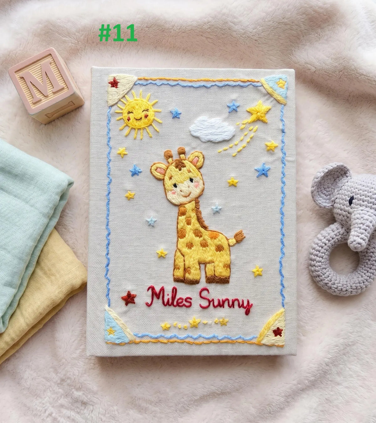 An embroidered baby book with a yellow giraffe, a smiling sun and stars — hand-embroidered by The Thread Nest