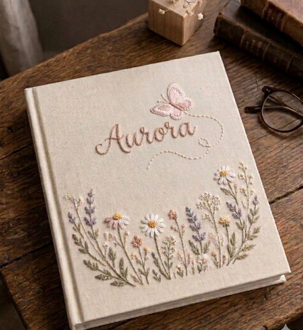 A beige journal with a name in cursive and a butterfly above it — hand-embroidered by The Thread Nest
